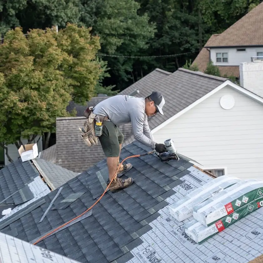 Charlotte Premier Roofing roofer running a nail gun along a shingle course beside stacked bundles