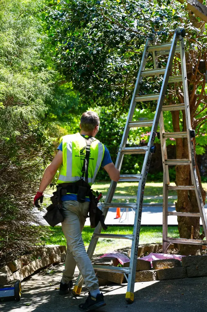 Charlotte Premier Roofing crew member in a hi-vis vest walking past two ladders set up in a driveway