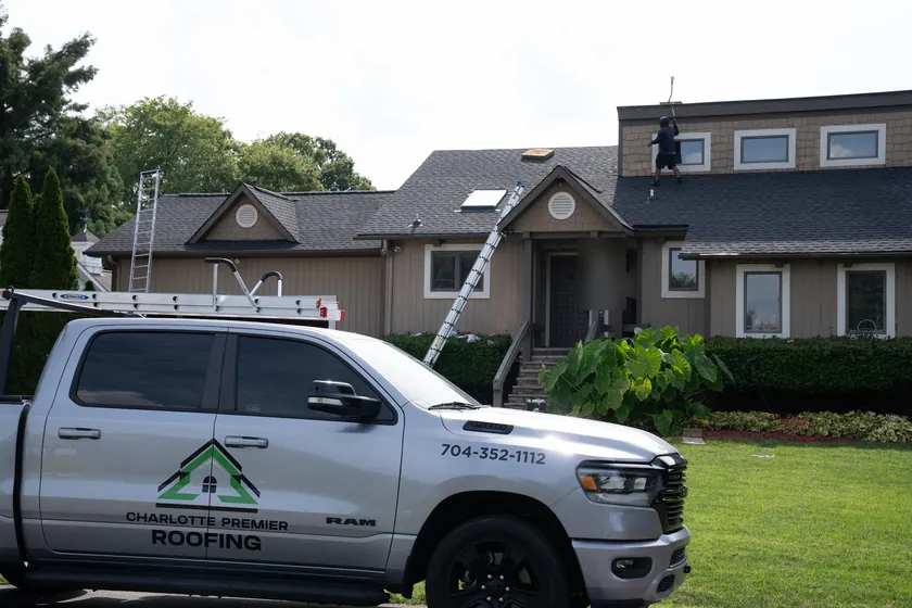 Charlotte Premier Roofing truck in front of a home in Cornelius while a crew member works on the roof