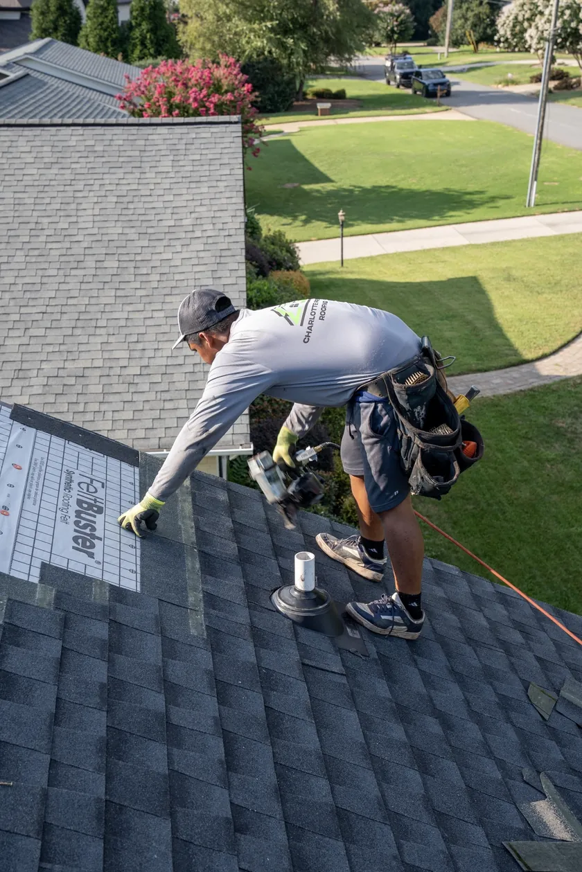 Charlotte Premier Roofing crew member nailing new architectural shingles around a pipe boot