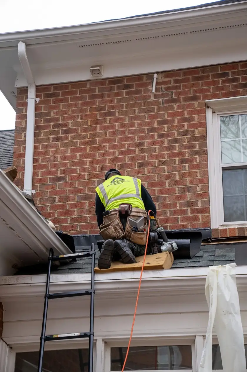 Charlotte Premier Roofing roofer working where a low roof meets a brick wall, ladder set at the eave