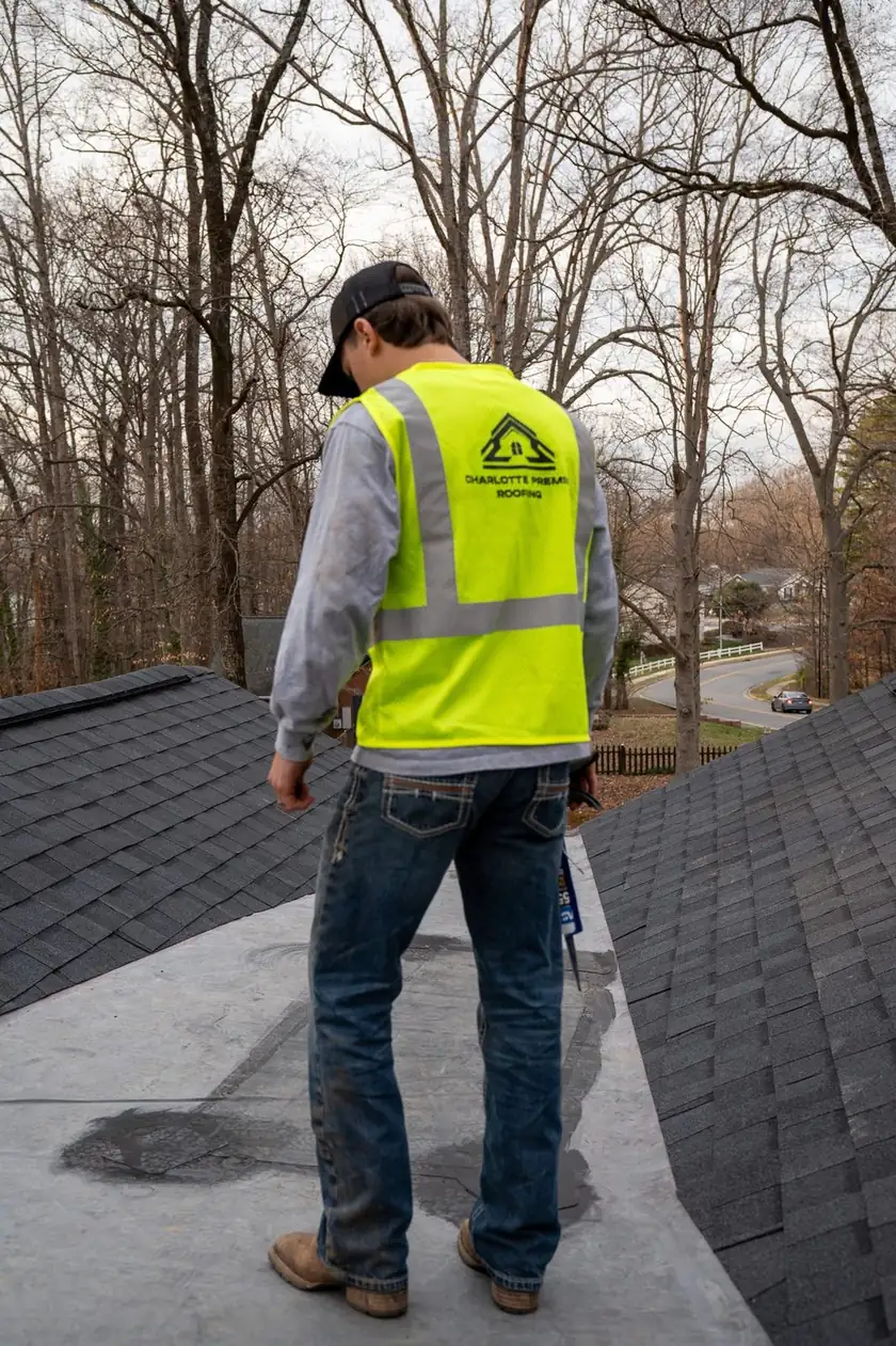 Charlotte Premier Roofing crew member with a tube of sealant on a low-slope roof section between two shingle slopes