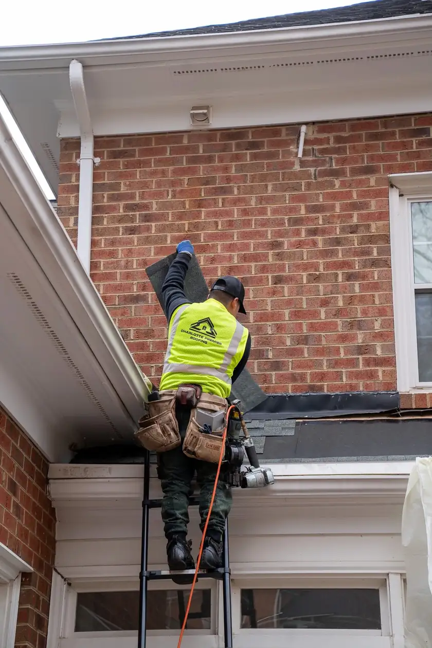 Charlotte Premier Roofing crew member on a ladder setting a shingle where a low roof meets a brick wall