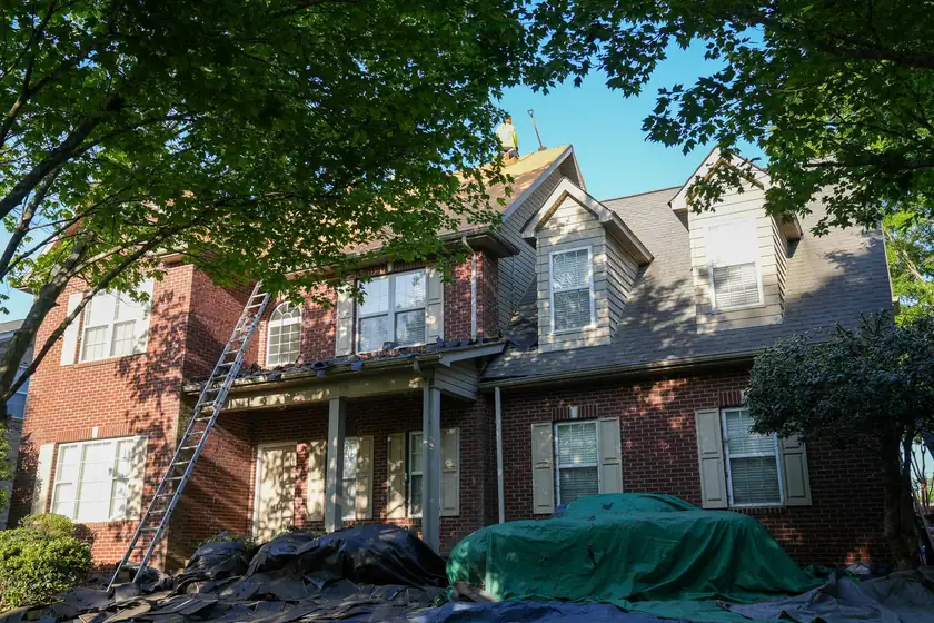Roof tear-off on a two-story brick home with tarps protecting the shrubs and driveway below