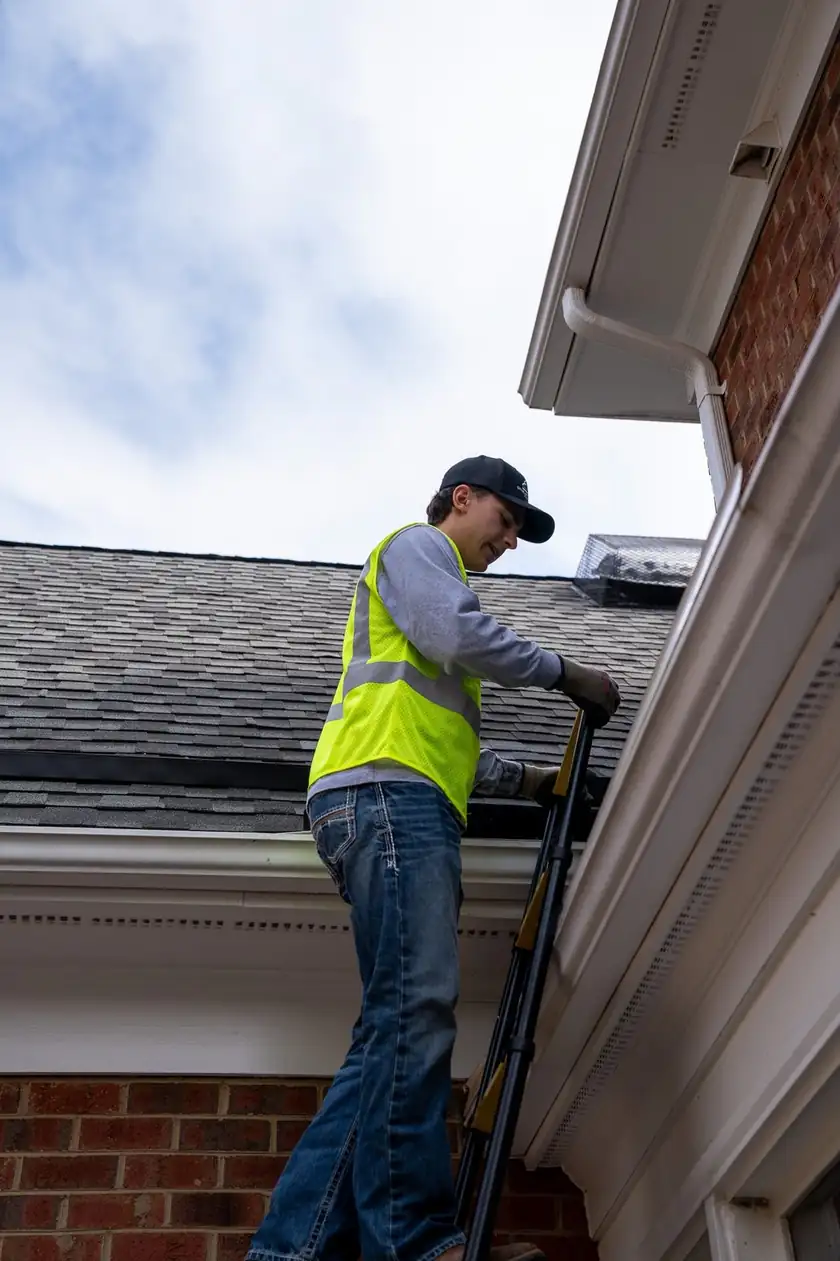 Charlotte Premier Roofing crew member climbing a ladder onto a shingle roof at the gutter line
