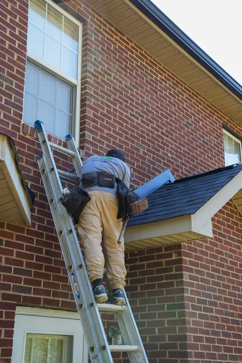 Charlotte Premier Roofing crew member on a ladder carrying drip edge up to a brick home's roof