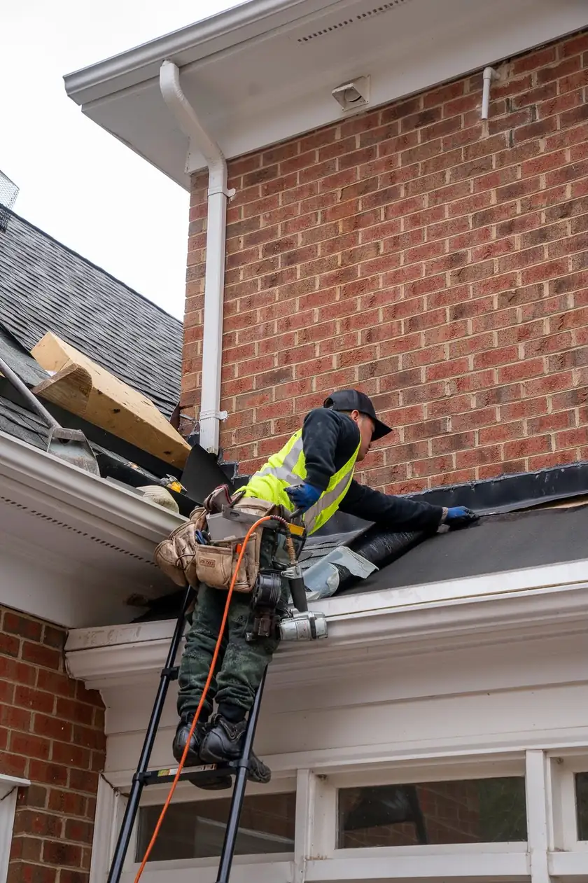 Charlotte Premier Roofing crew member laying a membrane strip where a low roof meets a brick wall