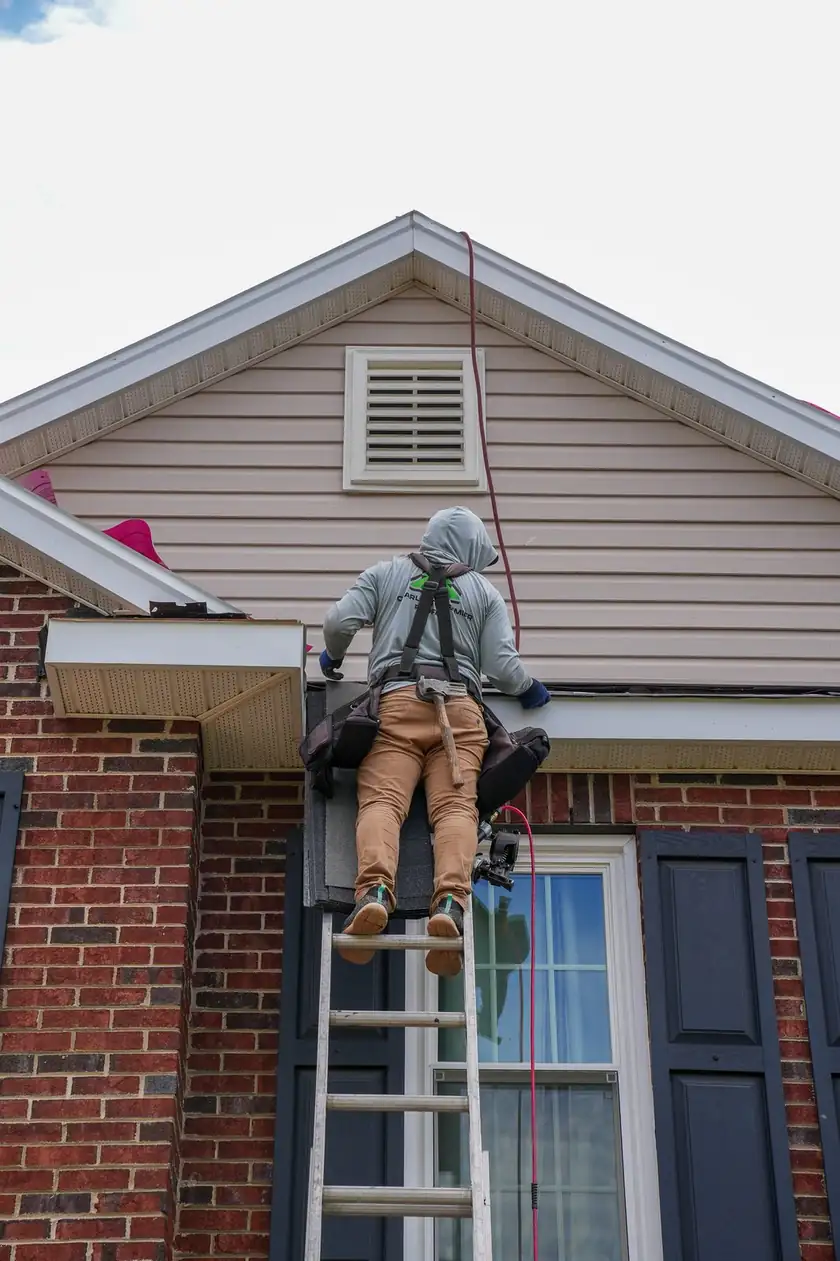 Charlotte Premier Roofing crew member on a ladder working shingles at the eave of a brick home