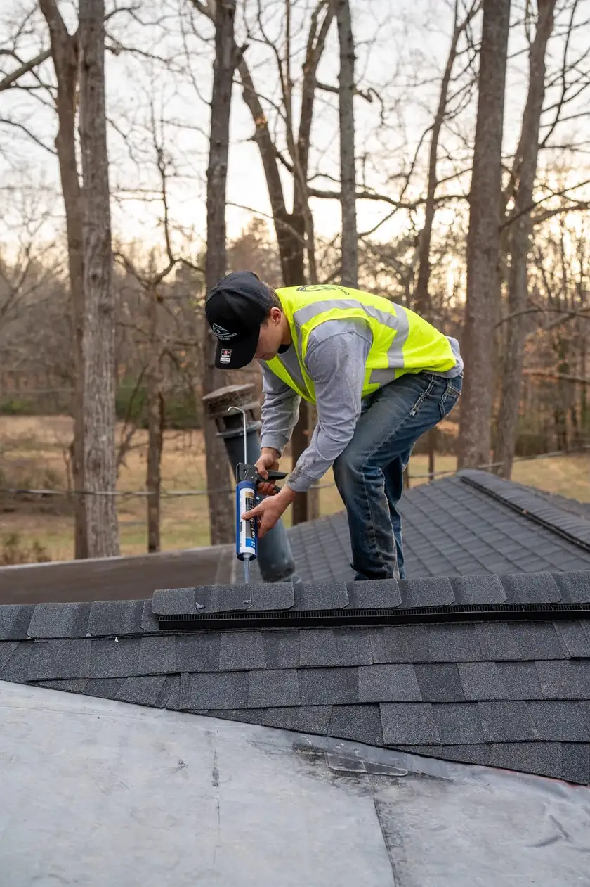 Charlotte Premier Roofing crew member running a bead of sealant along a ridge cap beside a vent pipe