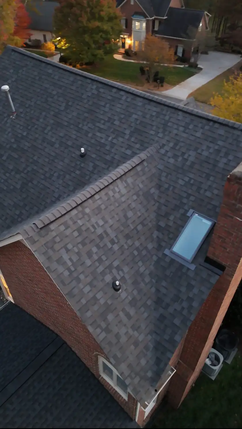 Aerial view of a finished architectural shingle roof with a skylight at dusk